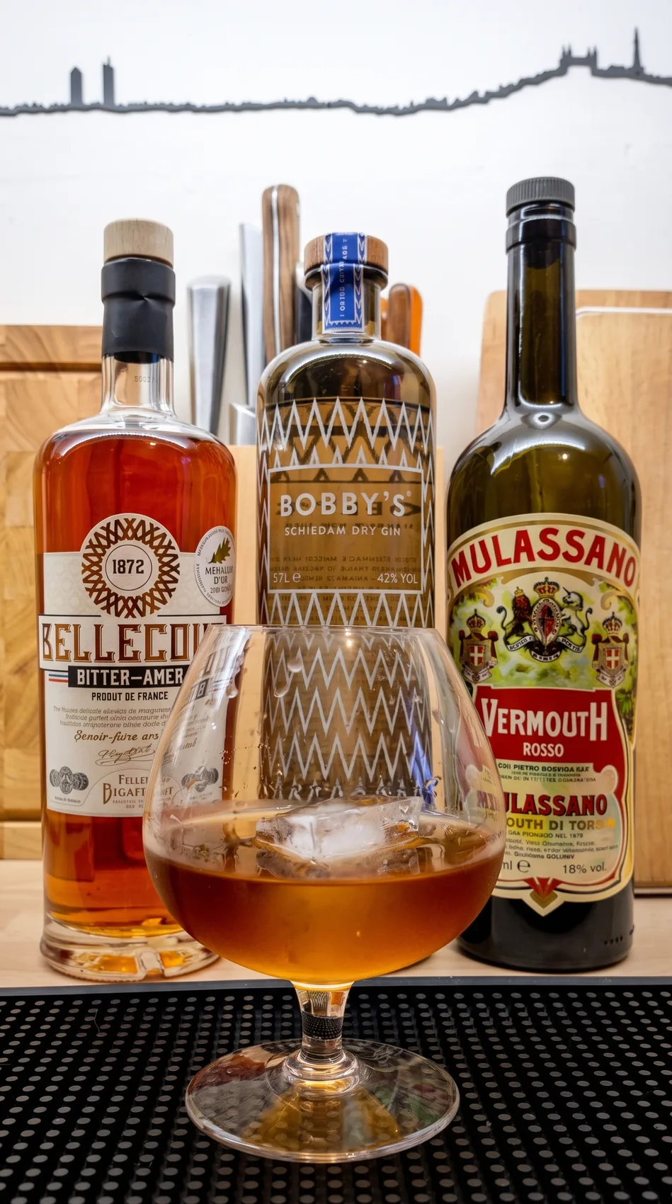 Un Negroni servi devant des bouteilles de bitter, de gin et de vermouth